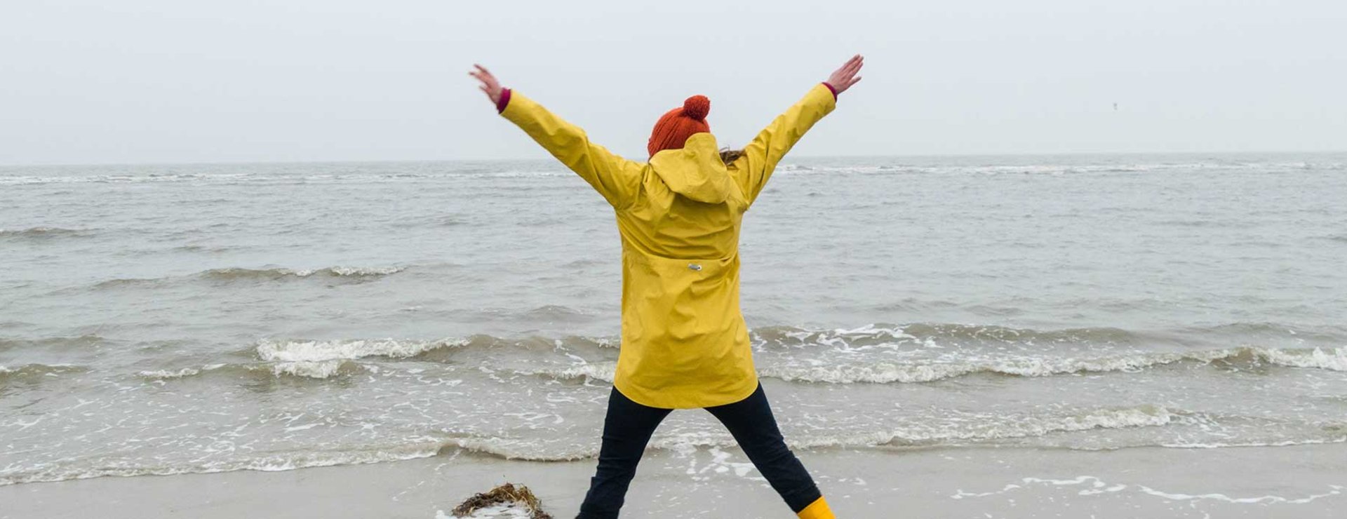 Frau springt in Regenjacke am regnerischen Meer